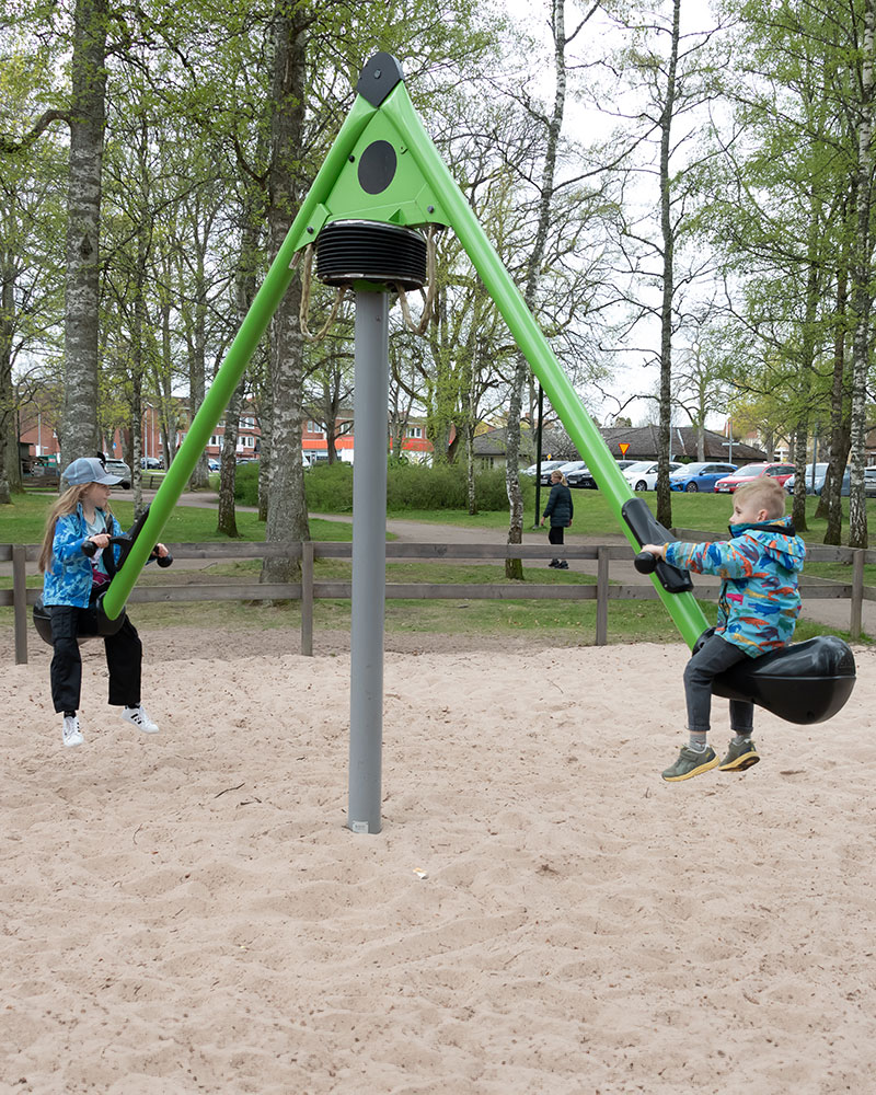 Children swing on a green Mobilus roundabout and seesaw.